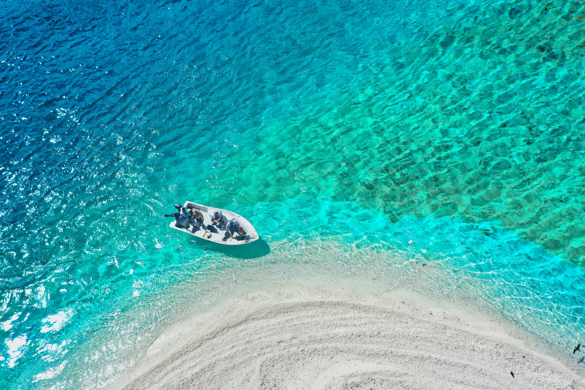 Boat anchored off a white sandbar in a turquoise lagoon